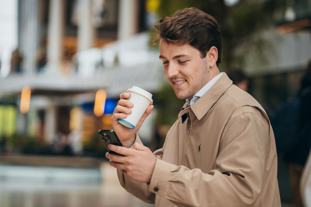 Man drinkt koffie en bekijkt zijn telefoon